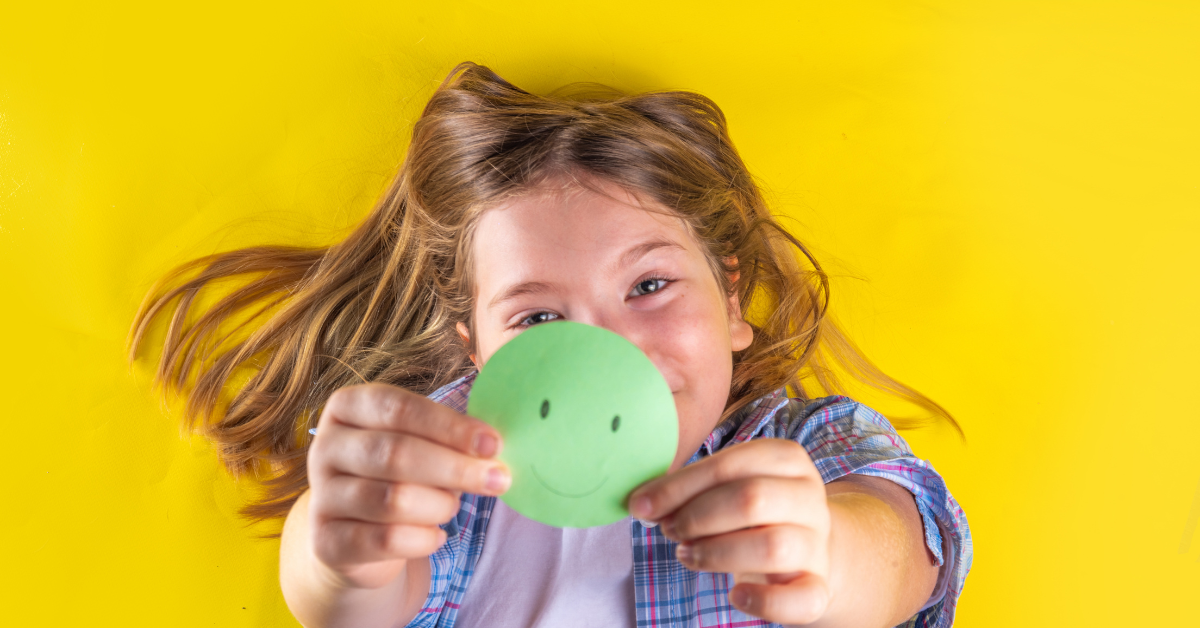 Child holding a smiley face cutout, symbolizing student mental health and wellbeing