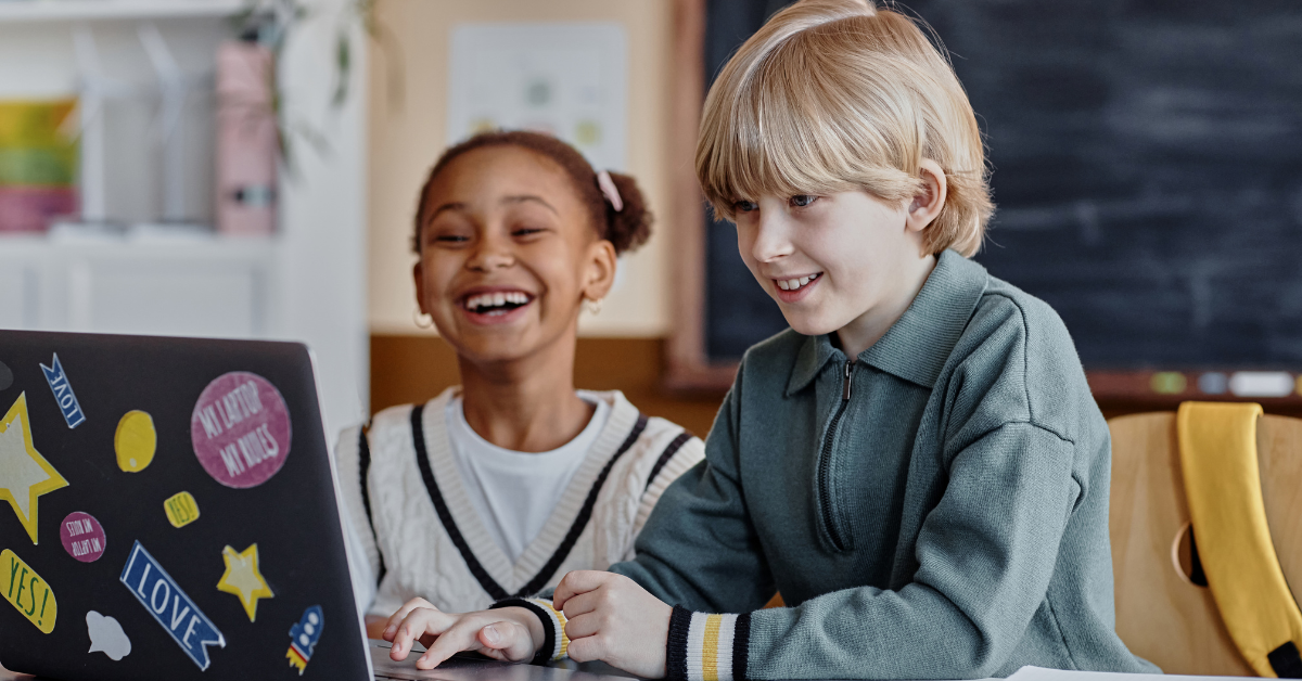 two young children looking at a laptop in the classroom