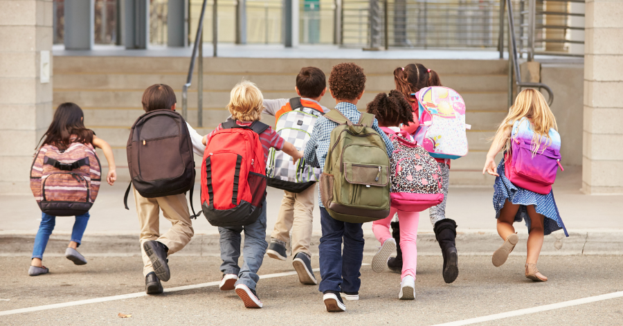 young children wearing backpacks running toward the front steps of school building