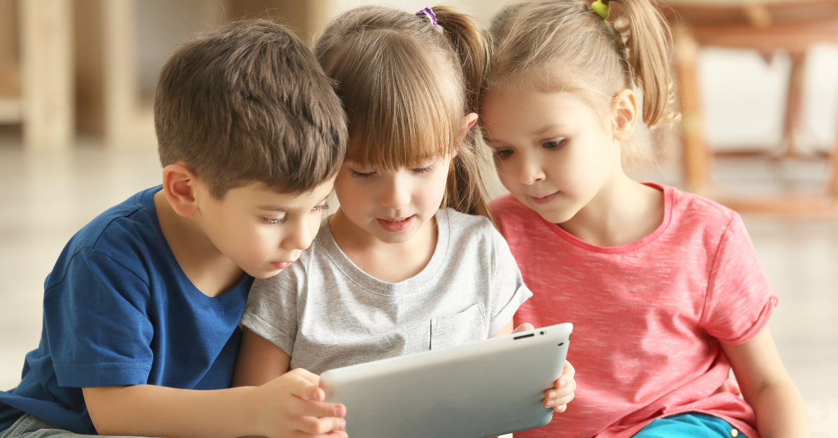 three young children look at a tablet