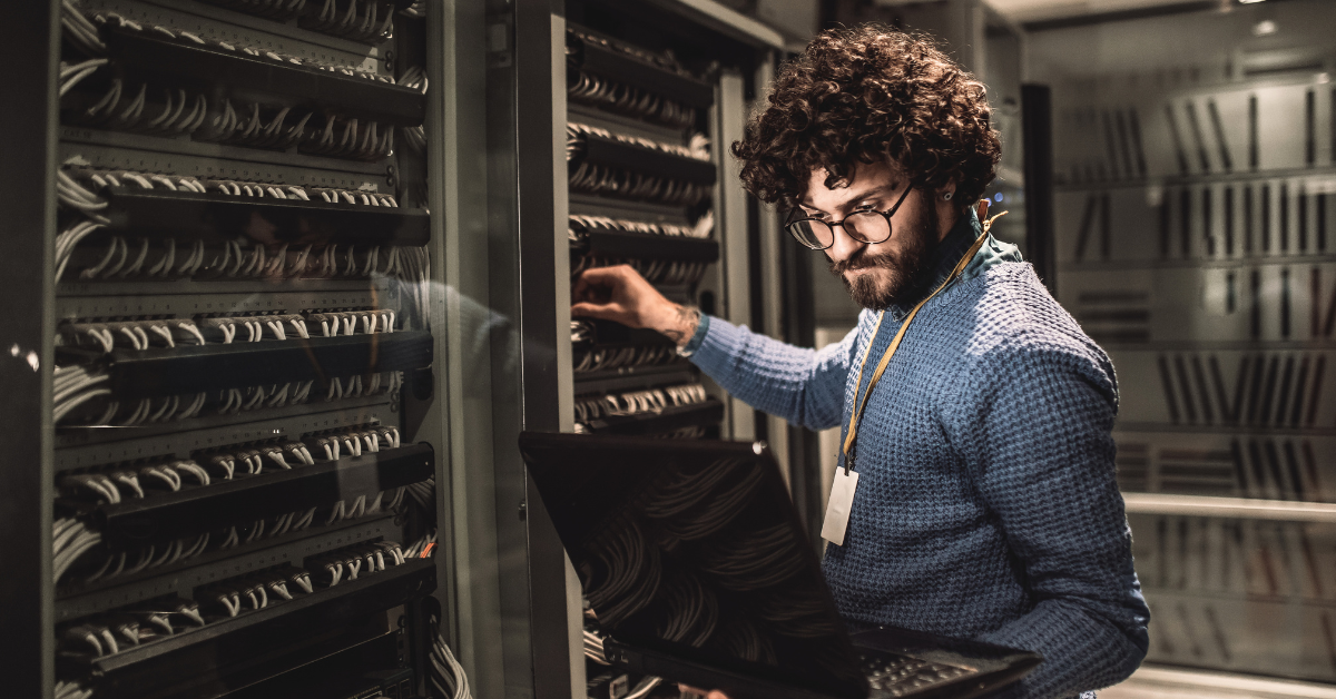 man stands in server room holding laptop